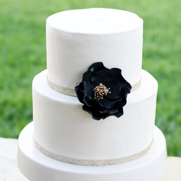 large black and gold open rose sugar flower on a two tier white fondant wedding cake